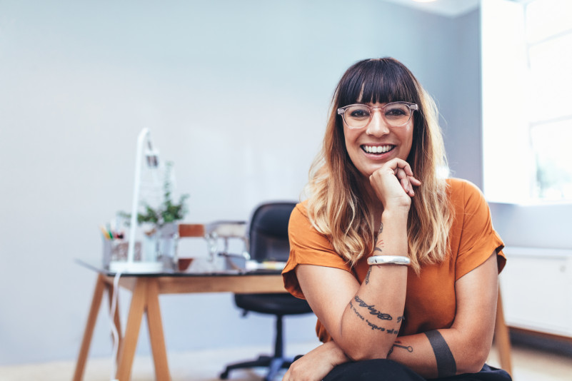 Illustrative image of a smiling young woman wearing glasses sitting in a pensive pose
